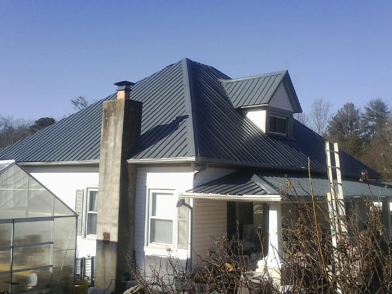Dark blue standing seam metal roof on a white farmhouse with dormer — Slate & Tile Roof Repair by Roofing Brothers in Fort Stewart