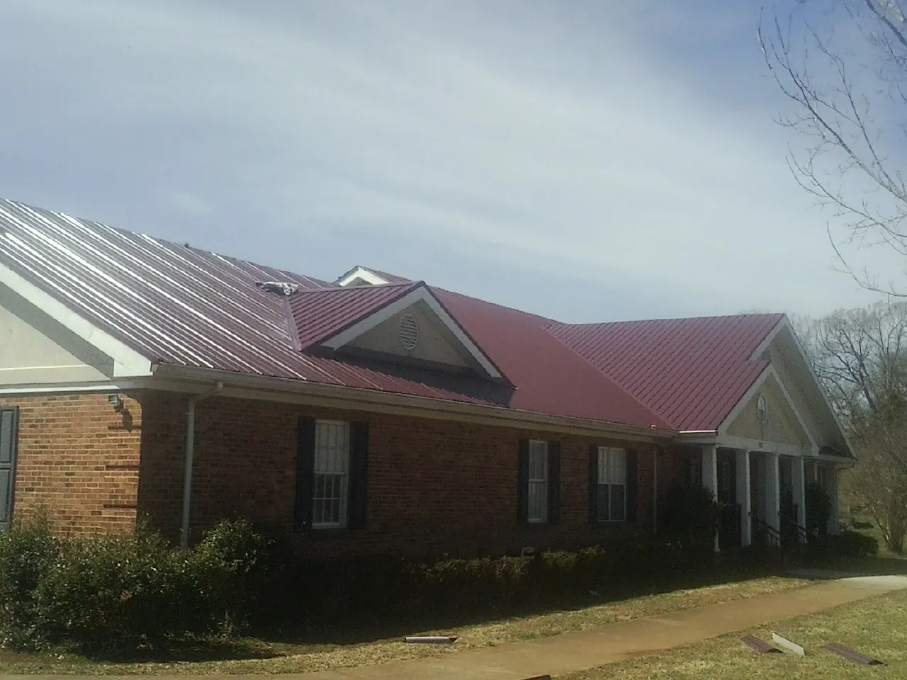 Red metal roof with gabled entries on a long brick building, from a Hail Damage Roof Repair job in Fort Stewart
