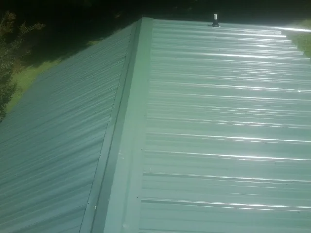 New green metal panels meeting at the ridge of a roof — Flat Roof Repair work by our crew in Fort Stewart