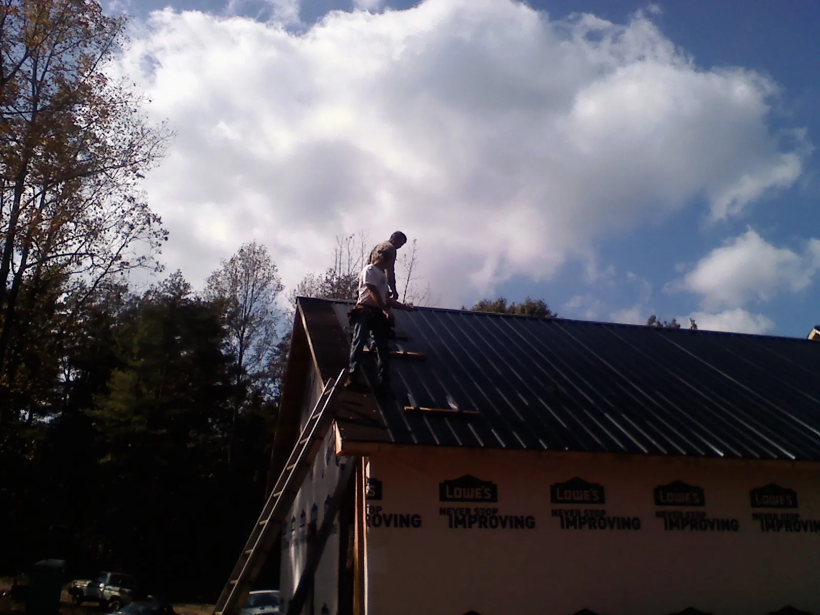 Roofer fastening dark metal panels high against a cloudy sky, from a Roof Inspection job in Fort Stewart
