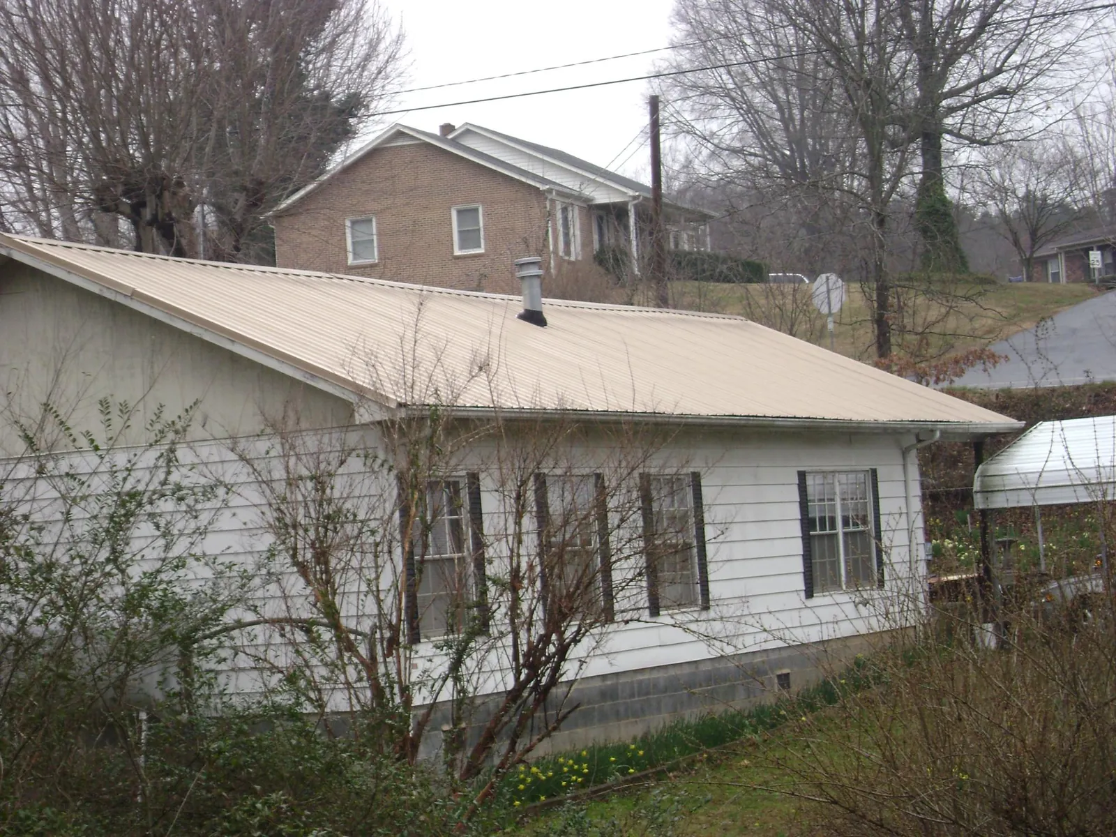 Tan metal roof on a white sided house set into a hillside — Commercial Roofing by Roofing Brothers in Fort Stewart